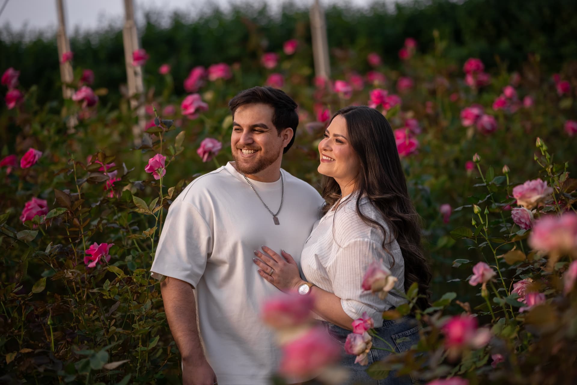 Monique e Thiago em meio a um roseiral cor-de-rosa