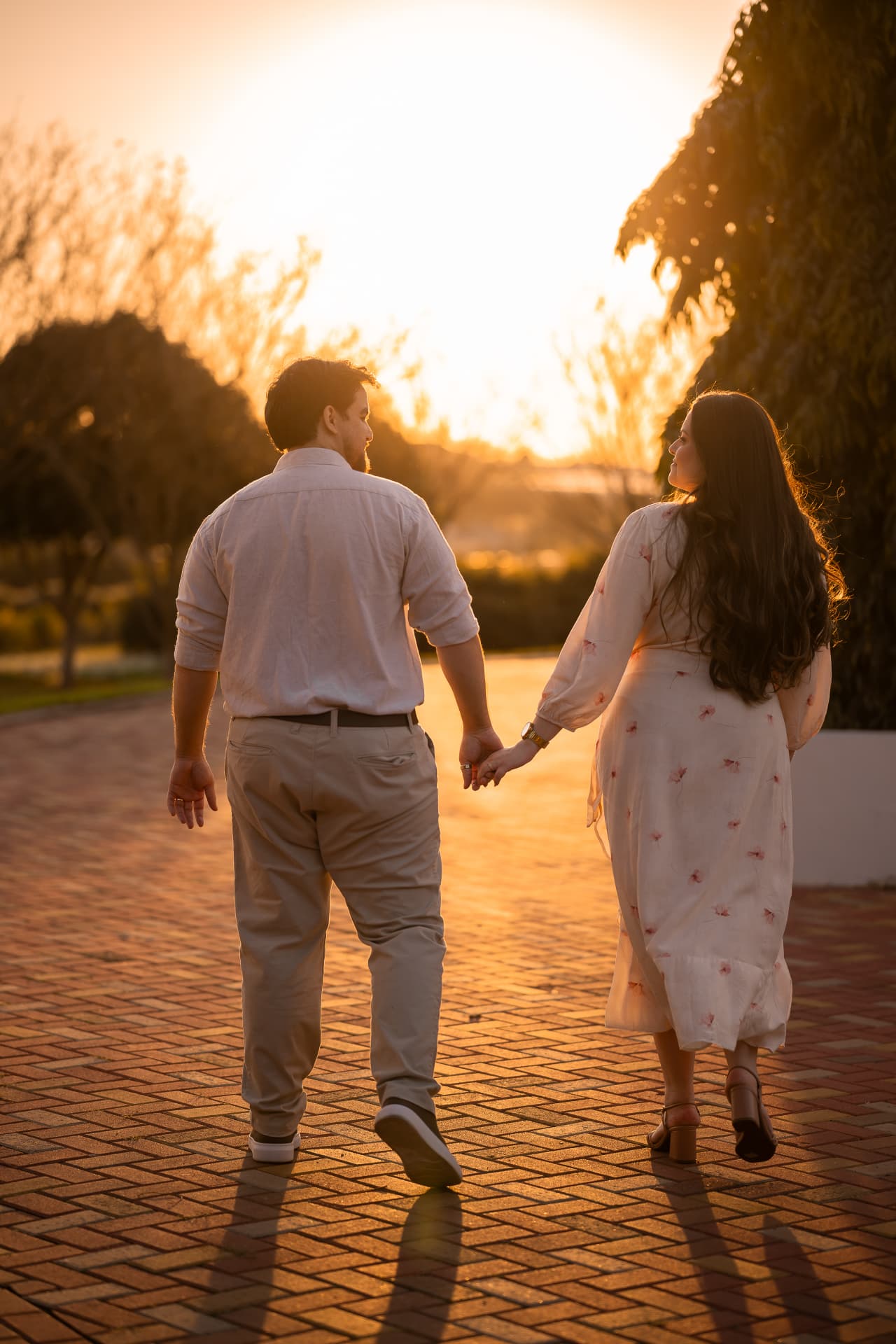 Monique e Thiago de mãos dadas caminhando de costas ao pôr do sol
